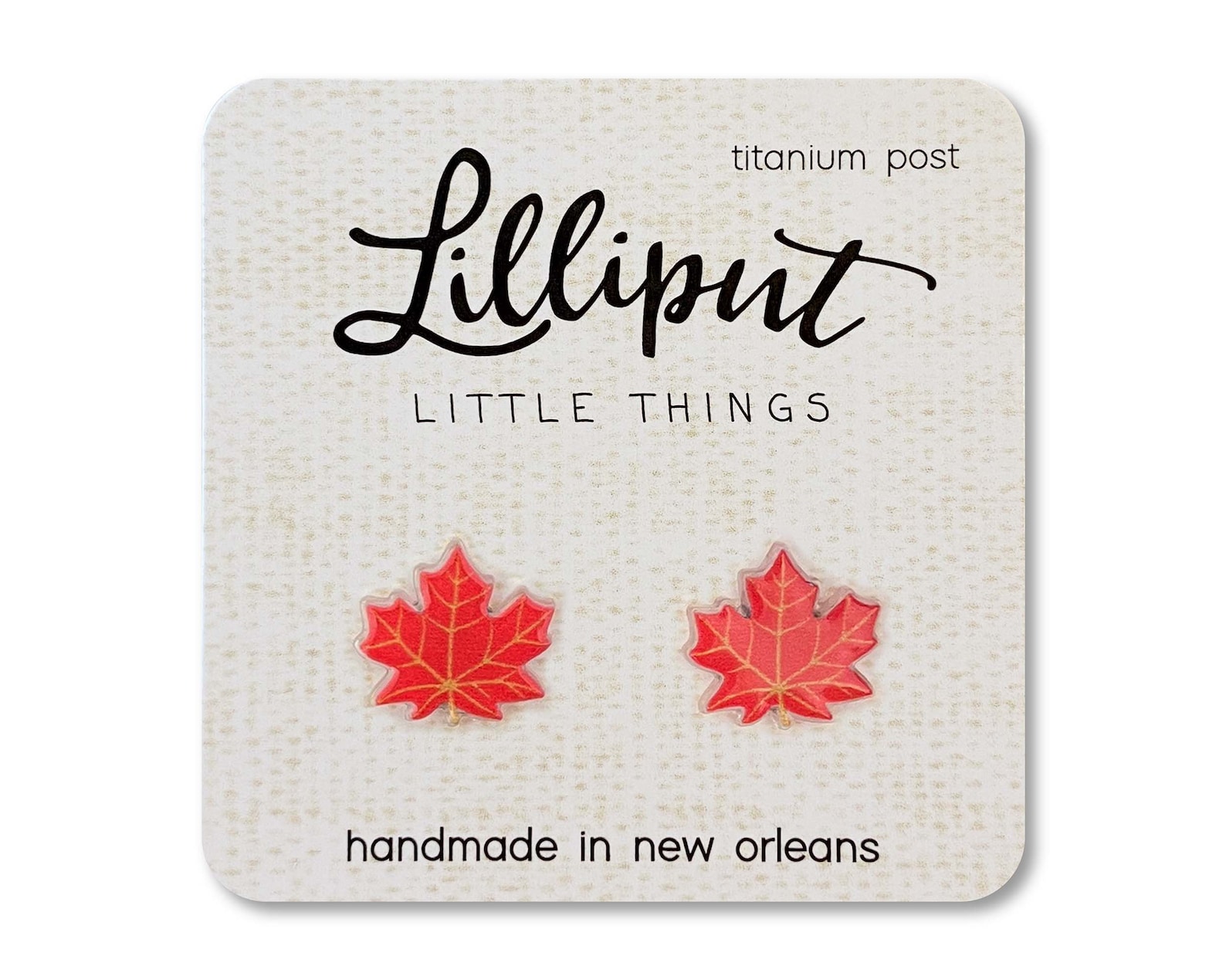 Two red maple leaf earrings on a white card