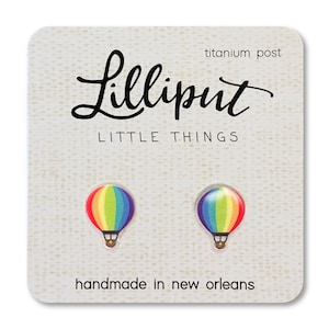 May include: A pair of rainbow hot air balloon stud earrings with titanium posts. The earrings are handmade in New Orleans and are packaged on a card with the text "Lilliputit Little Things".