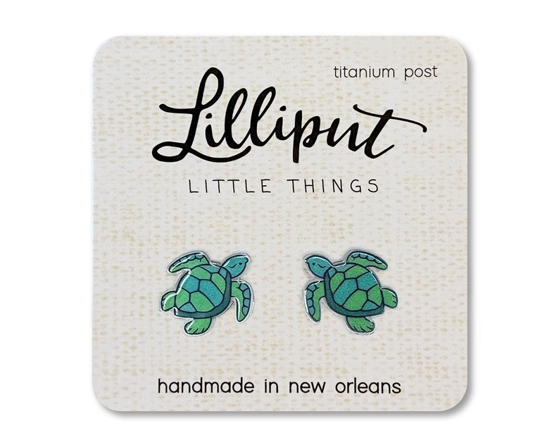 Acrylic stud earrings depicting a green and teal sea turtle. The earring card reads "Lilliput Little Things, handmade in New Orleans, titanium post"