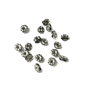 May include: A collection of silver-colored earring backs scattered on a white surface. The earring backs have a flower-like design with multiple petals and a small hole in the center. The backs are made of metal.