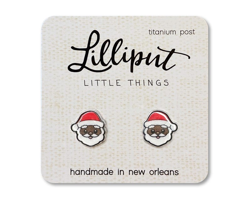 May include: A pair of earrings featuring a cartoon Santa Claus with a black face. The earrings are on a white card with the text "Lilliput Little Things" and "handmade in new orleans".