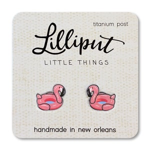 May include: A pair of pink flamingo inflatable pool float earrings with titanium posts. The earrings are handmade in New Orleans and feature the text "Lilliput Little Things" on the card.