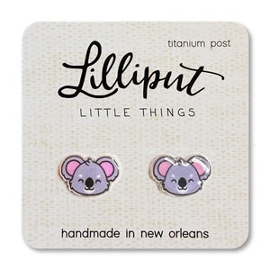 May include: A pair of silver koala earrings with pink ears and a white background. The earrings are on a card that says "Lilliput Little Things" and "handmade in New Orleans".