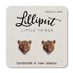 May include: A pair of leopard-print stud earrings on a white card. The card has the text "Lilliput LITTLE THINGS" in black script and "titanium post". The card also says "handmade in new orleans".
