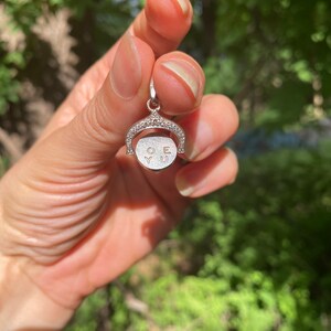 May include: A silver charm with a circle that rotates to reveal the words 'O.Y.U.' The charm is decorated with small, clear stones.