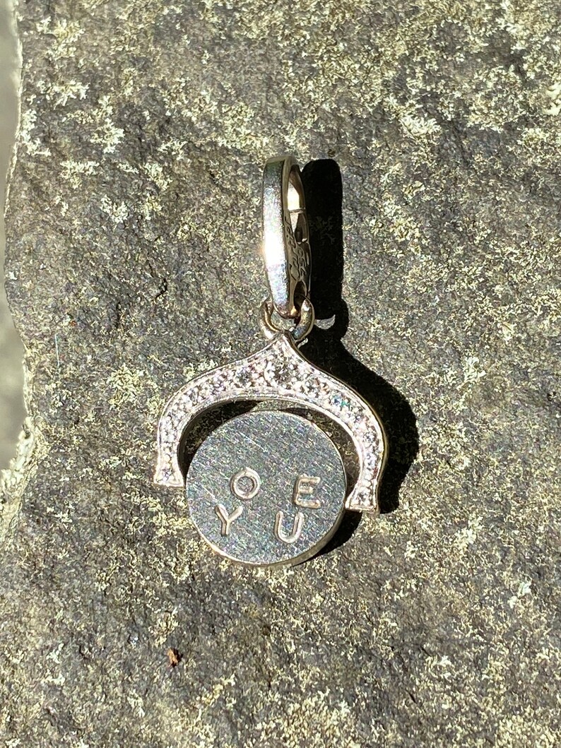 May include: A silver charm with a spinning disc that says 'LOVE YOU' in black lettering. The charm is decorated with small clear stones around the edge of the disc and the top of the charm.