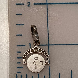 May include: A silver charm with a round disc featuring a circle, an arrow pointing up, and a number 1. The charm is attached to a silver loop.