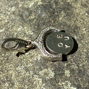 May include: A silver charm with a circular pendant that rotates. The pendant has the letters 'YOU' engraved on it. The charm has a silver clasp.