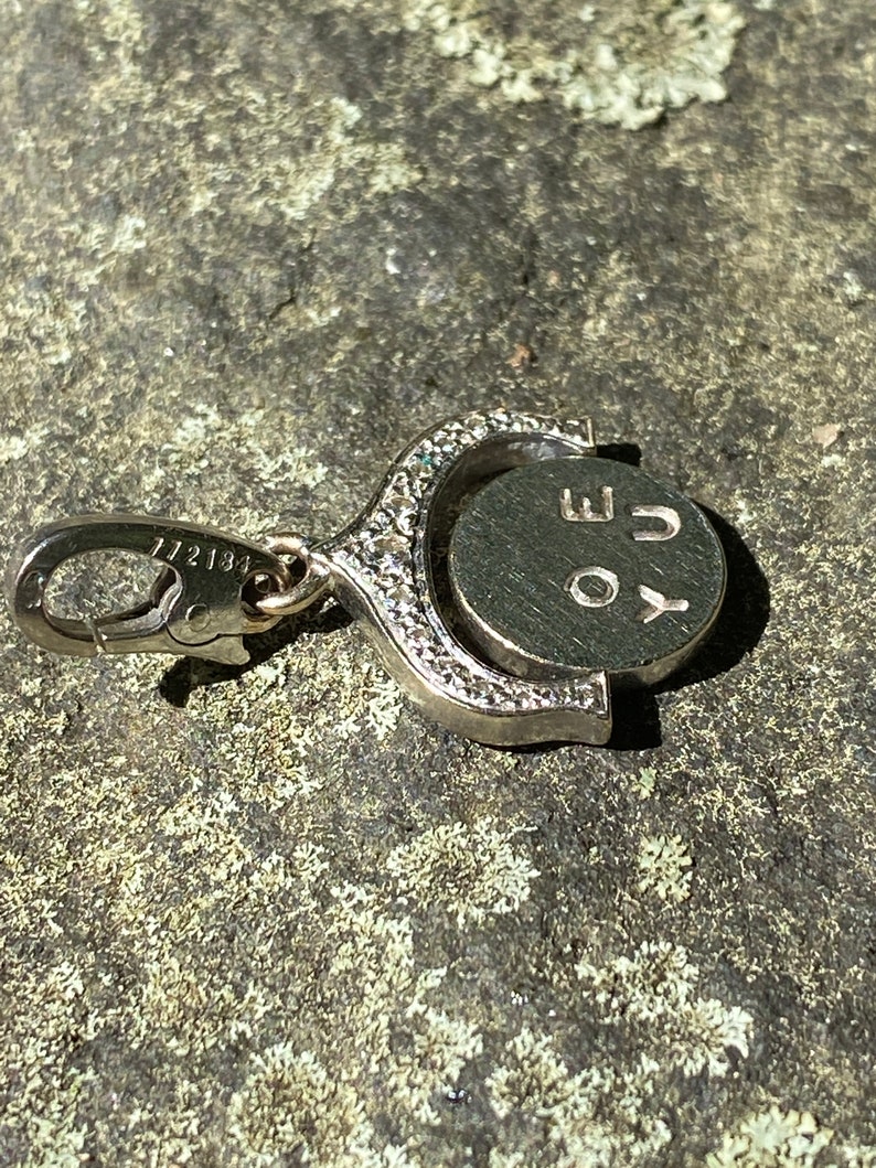 May include: A silver charm with a circular pendant that rotates. The pendant has the letters 'YOU' engraved on it. The charm has a silver clasp.