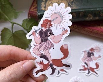 May include: A die-cut sticker featuring a person with reddish hair wearing a dark bodice and light-colored pants, holding a sword and a small flower. A sun-like emblem is behind their head, and they are standing on a fox with reddish-brown fur.