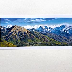 May include: A panoramic painting of a mountain range with snow-capped peaks. The mountains are painted in shades of blue, green, and brown, with a hint of purple in the valleys. The sky is a bright blue with fluffy white clouds.