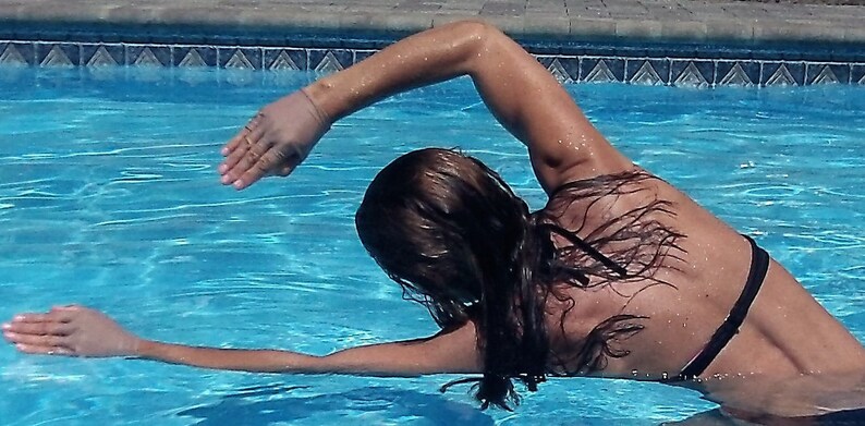 Puede incluir: Una mujer con un traje de ba&ntilde;o negro est&aacute; nadando en una piscina. Est&aacute; haciendo un ejercicio de espalda con el brazo extendido por encima del agua.