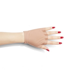 Puede incluir: Un par de guantes sin dedos de color carne con un primer plano de la mano que lleva los guantes. Las u&ntilde;as est&aacute;n pintadas de rojo brillante.