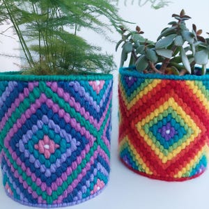 May include: Two colourful crocheted plant pots, one with a rainbow pattern and the other with a geometric pattern in shades of blue, green, and pink.
