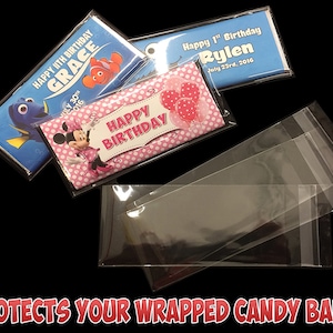 May include: Three clear plastic bags with a heat-sealed opening. The bags are designed to protect wrapped candy bars. The bags are lying on a black surface.