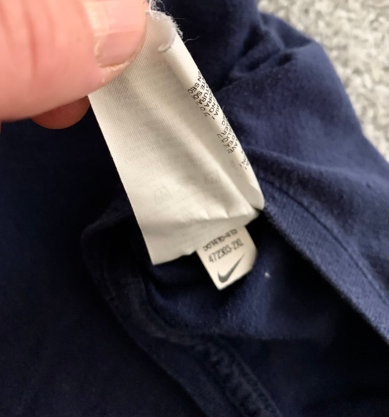 May include: Close-up of a navy blue garment with a white tag attached. The tag has text and a Nike logo. The tag reads "472303-2XL".