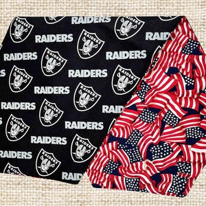 May include: Black and white fabric with the repeated text "RAIDERS" and a silver football helmet logo. The fabric is folded to reveal a red, white and blue fabric with a pattern of American flags.