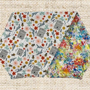 May include: Two fabric table runners, one with a white background and a repeating pattern of beehives, flowers, and bees, and the other with a white background and a colorful splatter paint design.