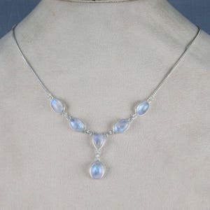 May include: A silver necklace featuring oval-shaped, iridescent moonstone gemstones. The necklace has a delicate chain and a pendant with a teardrop-shaped moonstone. The gemstones have a soft, milky blue color.