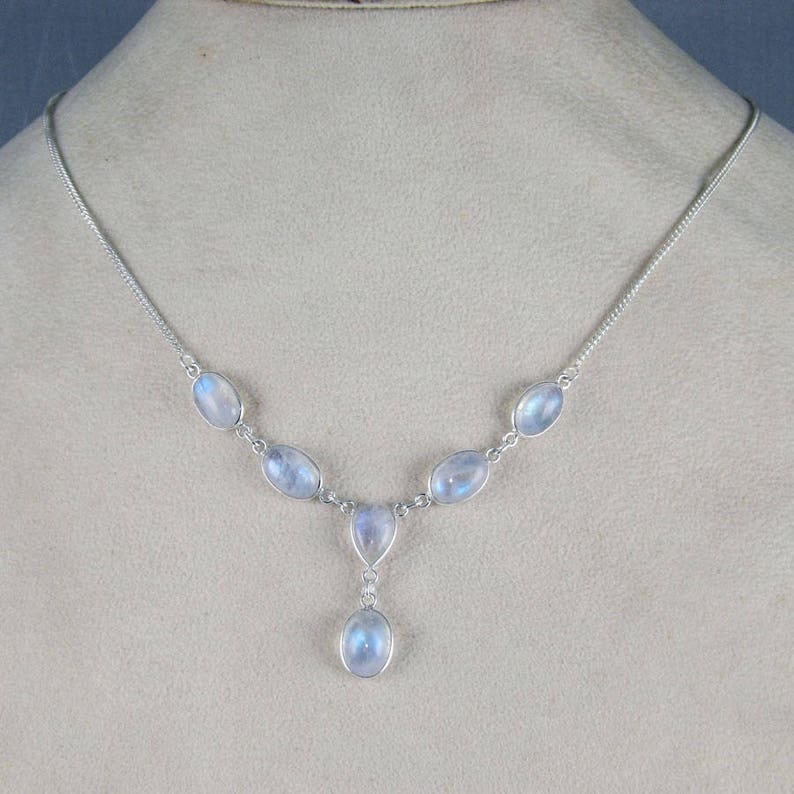 May include: A silver necklace featuring oval-shaped, iridescent moonstone gemstones. The necklace has a delicate chain and a pendant with a teardrop-shaped moonstone. The gemstones have a soft, milky blue color.