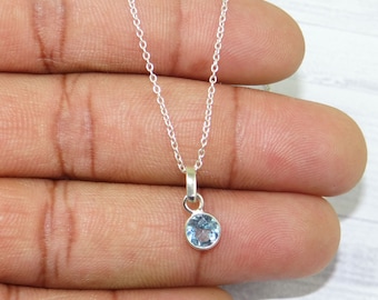 May include: A delicate silver chain necklace with a small, round, light blue gemstone pendant.