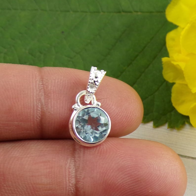May include: A silver pendant with a light blue gemstone. The pendant has a detailed design with a small loop at the top for attaching to a chain.