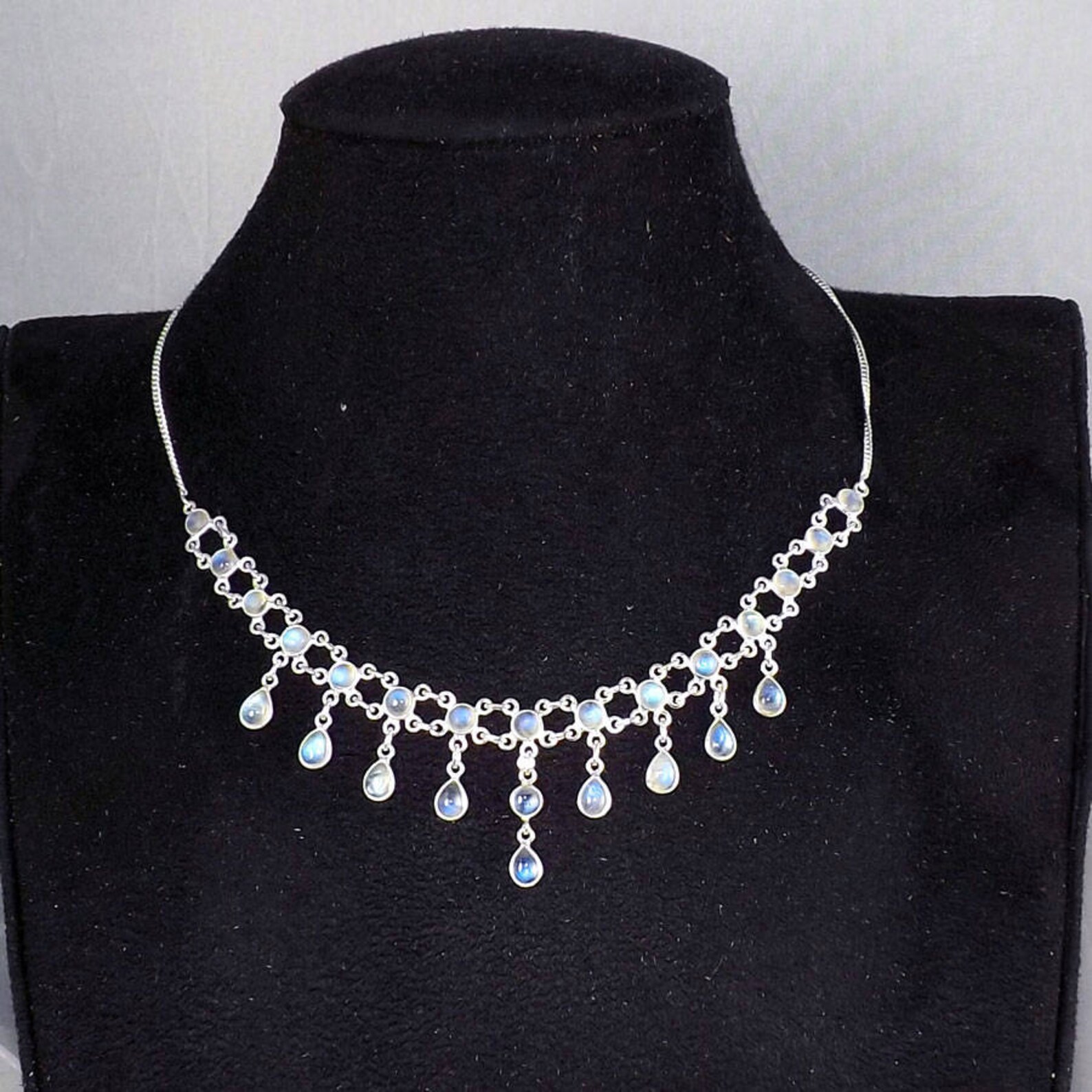Rainbow moonstone necklace with round and teardrop stones in sterling silver, displayed on a black velvet bust.