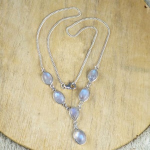 May include: A silver necklace featuring oval and teardrop-shaped moonstone pendants. The chain is a delicate curb link, and the necklace has a lobster clasp closure. The moonstones have a soft, iridescent glow, and the necklace is displayed on a wooden surface.