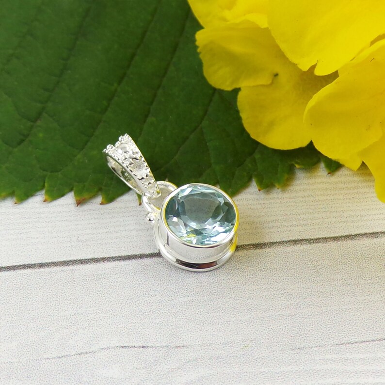 May include: A silver pendant with a light blue gemstone set in a bezel setting. The pendant has a decorative crown-like bail with small clear stones.
