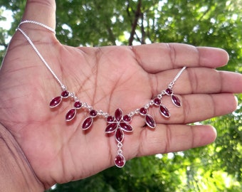 May include: A silver necklace with a red gemstone flower pendant and dangling red gemstone drops.