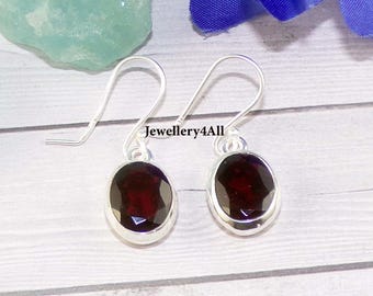 May include: Silver earrings featuring oval, deep red gemstones. The earrings have a simple hook design and are set in a silver bezel. The text "Jewellery4All" is visible. The background includes blue and green elements.