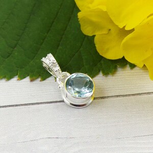 May include: A silver pendant with a light blue gemstone set in a bezel setting. The pendant has a decorative crown-like bail with small clear stones.
