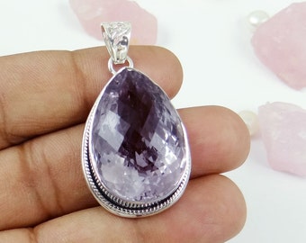 May include: A teardrop-shaped pendant with a large, faceted, light purple gemstone. The gemstone is set in a silver-colored metal frame with a decorative rope-like border. The bail is also silver-colored and has a textured design.