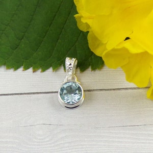 May include: A silver pendant with a light blue gemstone. The pendant has a detailed design around the edge of the gemstone.