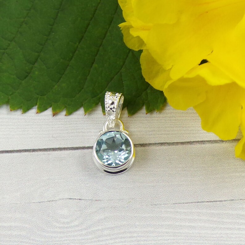 May include: A silver pendant with a light blue gemstone. The pendant has a detailed design around the edge of the gemstone.