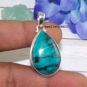 Op de afbeelding: Een traanvormige hanger met een blauwgroene edelsteen gezet in sterling zilver. De edelsteen heeft een gemarmerd patroon met zwarte aderen.