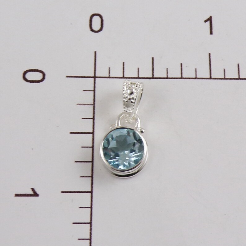 May include: A silver pendant with a light blue oval gemstone. The pendant is about 1 inch long.