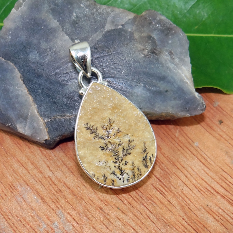 May include: A teardrop-shaped pendant with a silver bail and a beige stone featuring a black dendritic pattern.