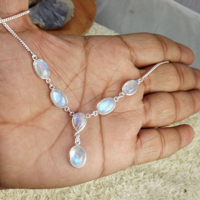 May include: A silver necklace featuring oval and teardrop-shaped moonstone gemstones. The necklace has a delicate chain and is designed with a series of bezel-set stones, creating a Y-shaped pendant. The moonstones display a soft, iridescent glow.