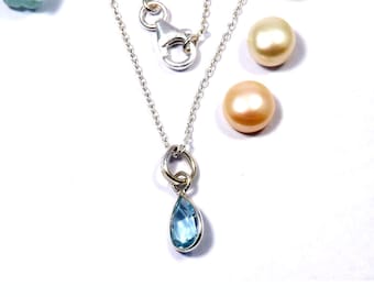 May include: A silver chain necklace with a teardrop-shaped blue gemstone pendant. The pendant is attached to a silver ring.