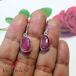 May include: A pair of silver dangle earrings with pink gemstone drops. The earrings have a simple design and are perfect for everyday wear.