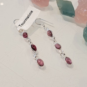 May include: A pair of silver earrings with pink tourmaline stones. The earrings have a dangle design with four stones on each earring. The tag says "Tourmaline".