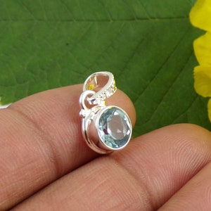 May include: A silver pendant with a light blue gemstone. The pendant has a delicate, swirling design.