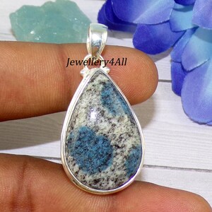 Puede incluir: Un colgante de plata con una piedra azul y blanca en forma de lágrima y una anilla de plata. La piedra tiene un patrón moteado con motas azules y blancas.