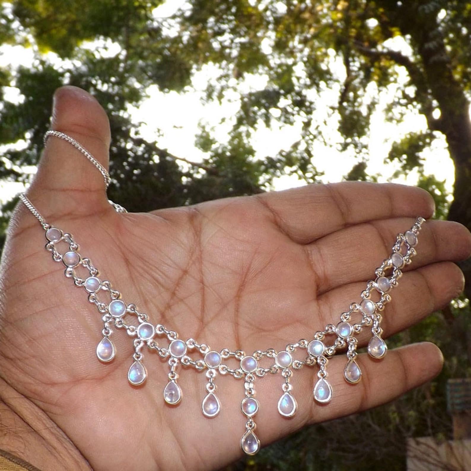 Hand holding a sterling silver necklace with round and teardrop rainbow moonstones.