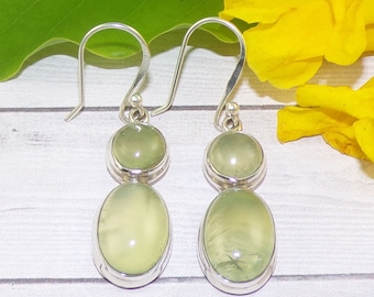 May include: A pair of silver dangle earrings with two green gemstones on each earring. The top gemstone is round and the bottom gemstone is oval.