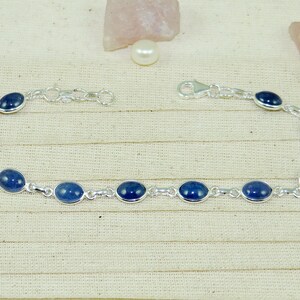 May include: A silver bracelet with oval-shaped blue gemstones. The bracelet has a lobster clasp closure.