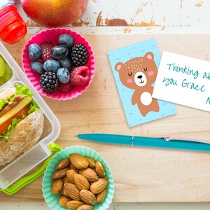 May include: A lunchbox with a sandwich, grapes, and almonds. A pink container with blueberries and raspberries. A blue and brown card with a cartoon bear and the text "Thinking about you Grace Mom".