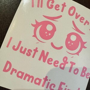 May include: A white sticker featuring pink text and cartoon eyes. The text says "I'll Get Over It, I Just Need To Be Dramatic First". The eyes are large and stylized, with eyelashes and star-shaped highlights.