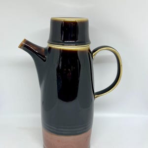 Puede incluir: Una jarra de cerámica marrón con un borde dorado y una base marrón y roja.